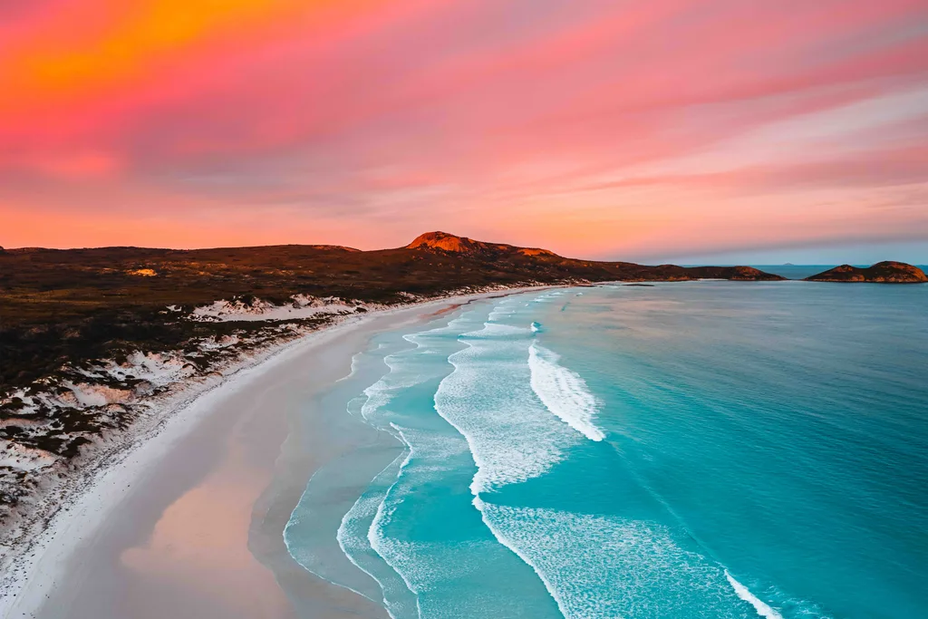 blue coastline of Lucky bay in WA with white sand and pink sky.