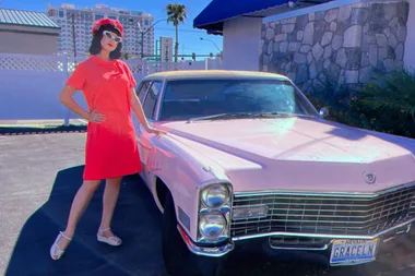 Rochelle Anvik, who has a passion for all things from the 1050s poses in a red frock and matching hat, next to her vintage pink car