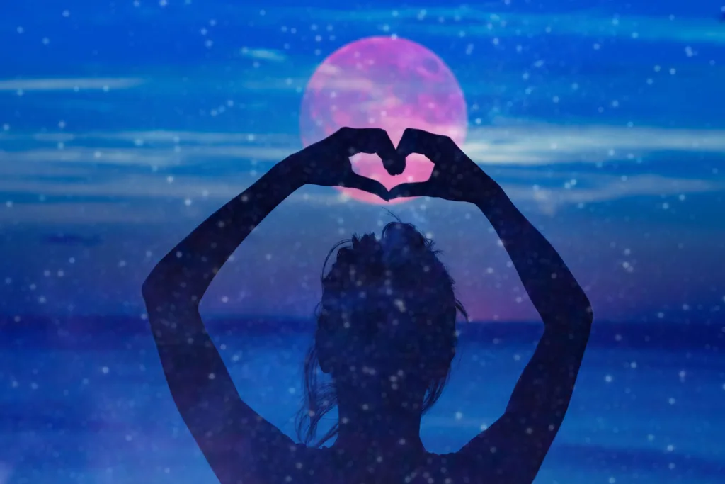 A graphic of a woman holding hands up above her head in the shape of a heart in front of the moon.