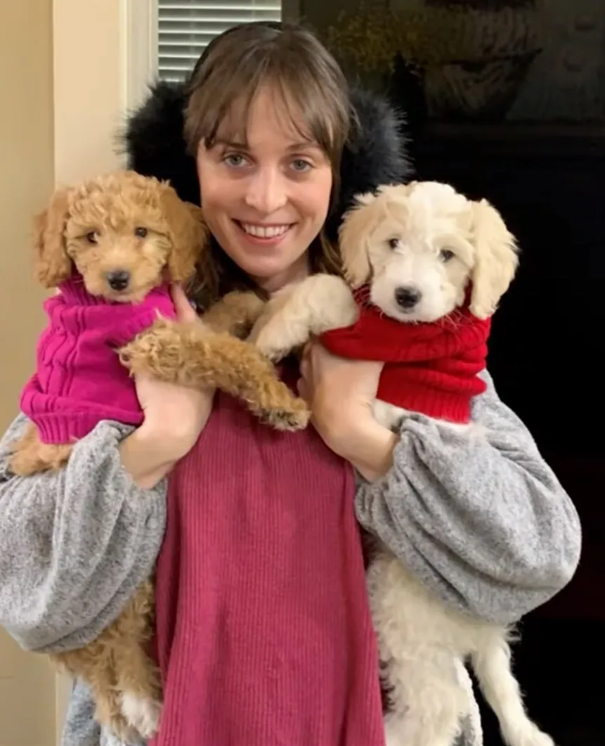 Woman in red jumper holding two dogs with jumpers on