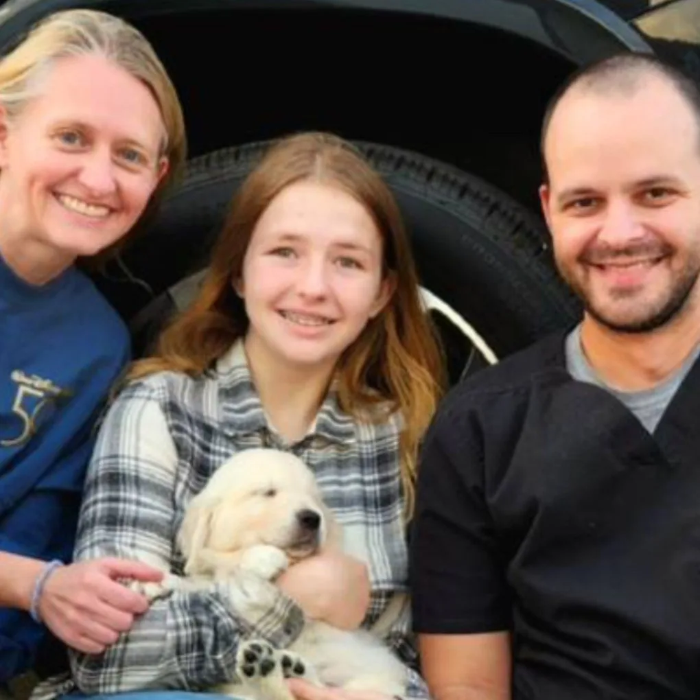 Carly wears a plaid shirt standing between her mum, wearing a blue shirt and dad wearing a black shirt