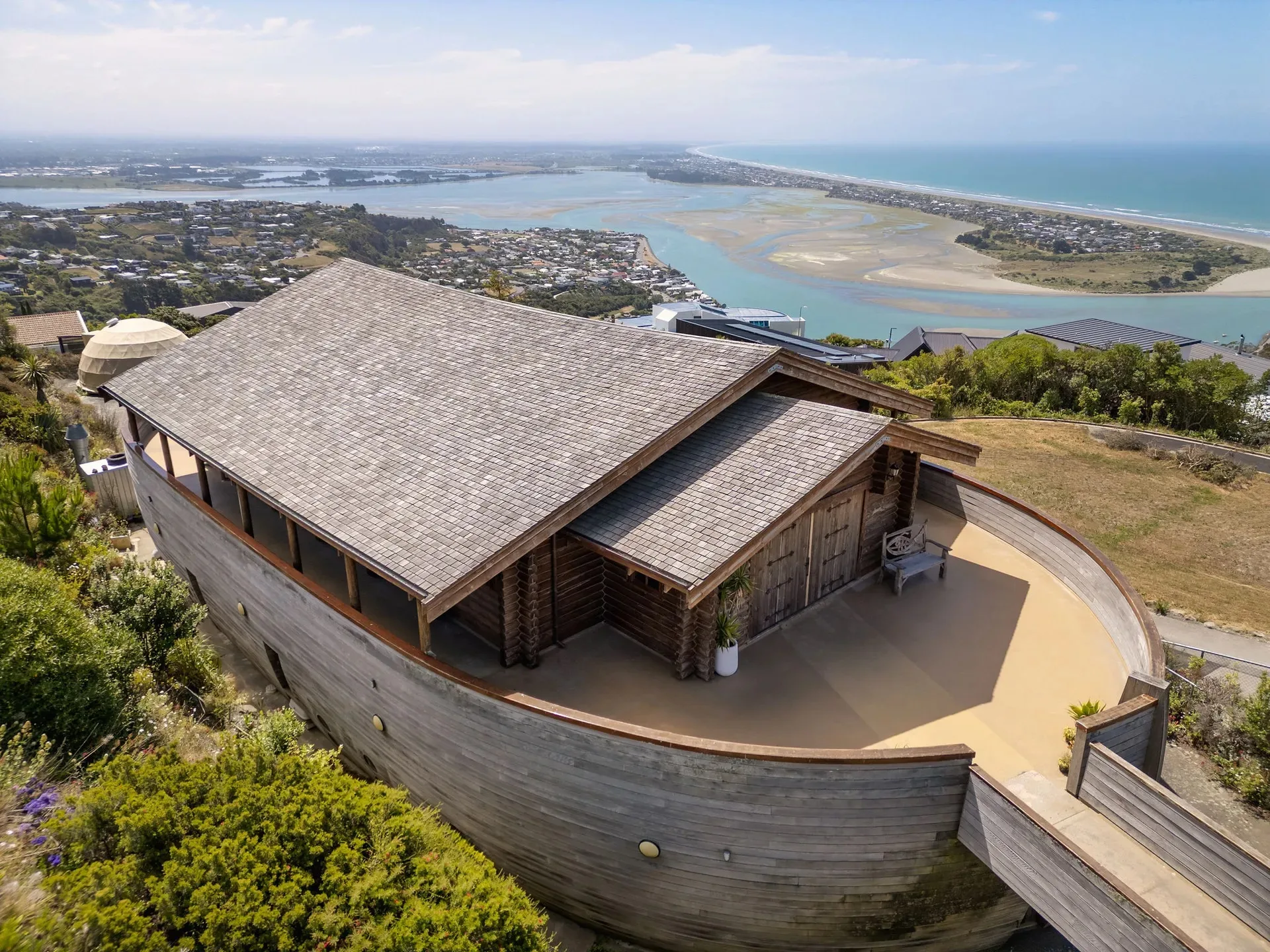 Wooden life sized ark structure outside with houses and sea in the background.
