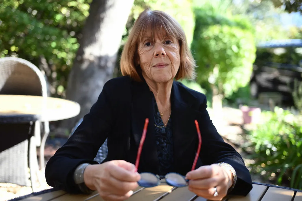 Gisele Pelicot sat in black jacket holding red glasses