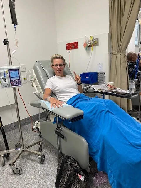 Claire in hospital. She is sitting in a hospital bed with a blue blanket on her lap.