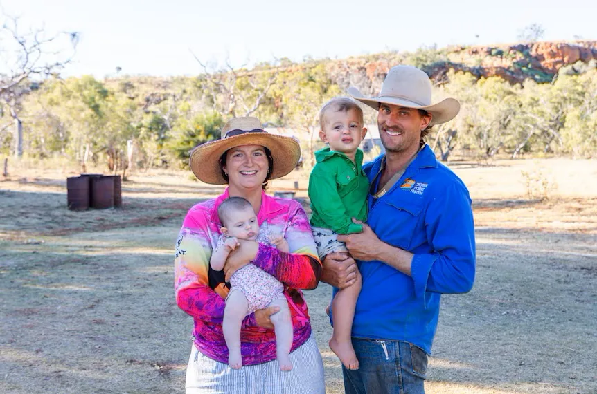 woman in colourful top and white hat holding baby, man in blue shirt and white hat holding child in green .