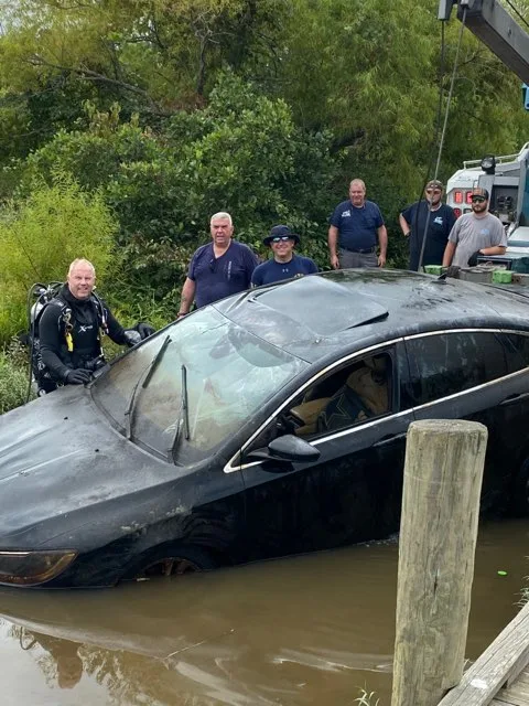 Image of underwater detectives standing around a sunken car