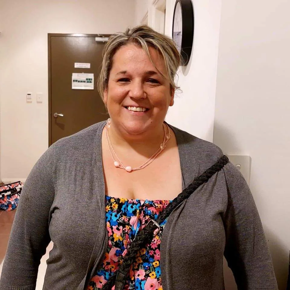 Nicole smiling at the camera. She is wearing a floral print shirt and a grey cardigan.