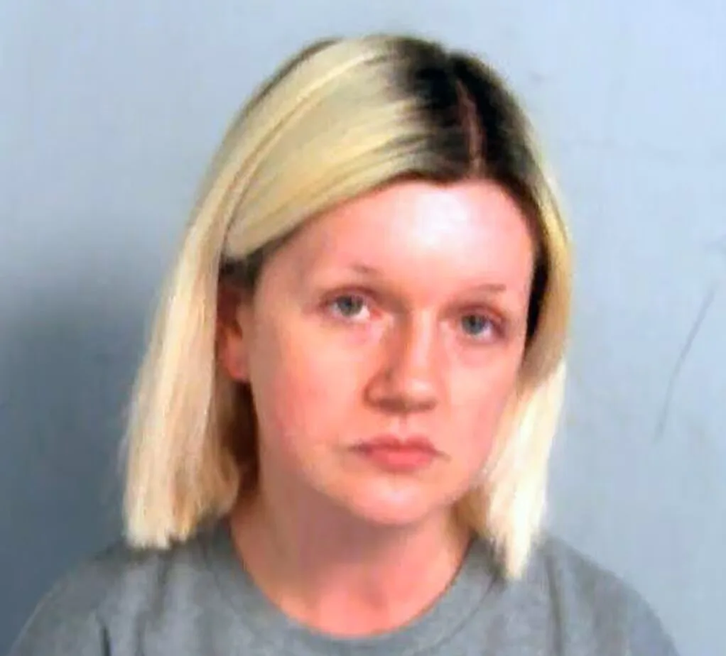 A woman with blonde hair stares at the camera. She is wearing a grey t-shirt