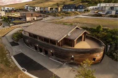 Wooden life sized ark structure outside with houses in the background.