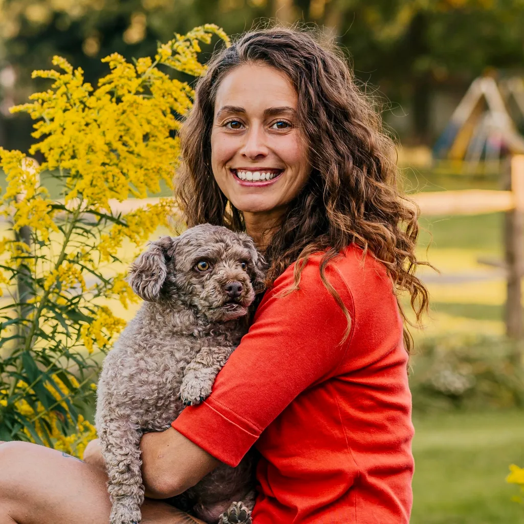 Image of woman wearing orange top and holding poodle dog