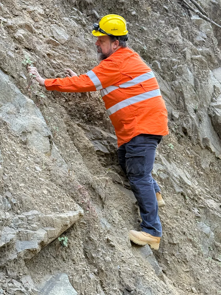 Image of man wearing orange hi vis and checking rock