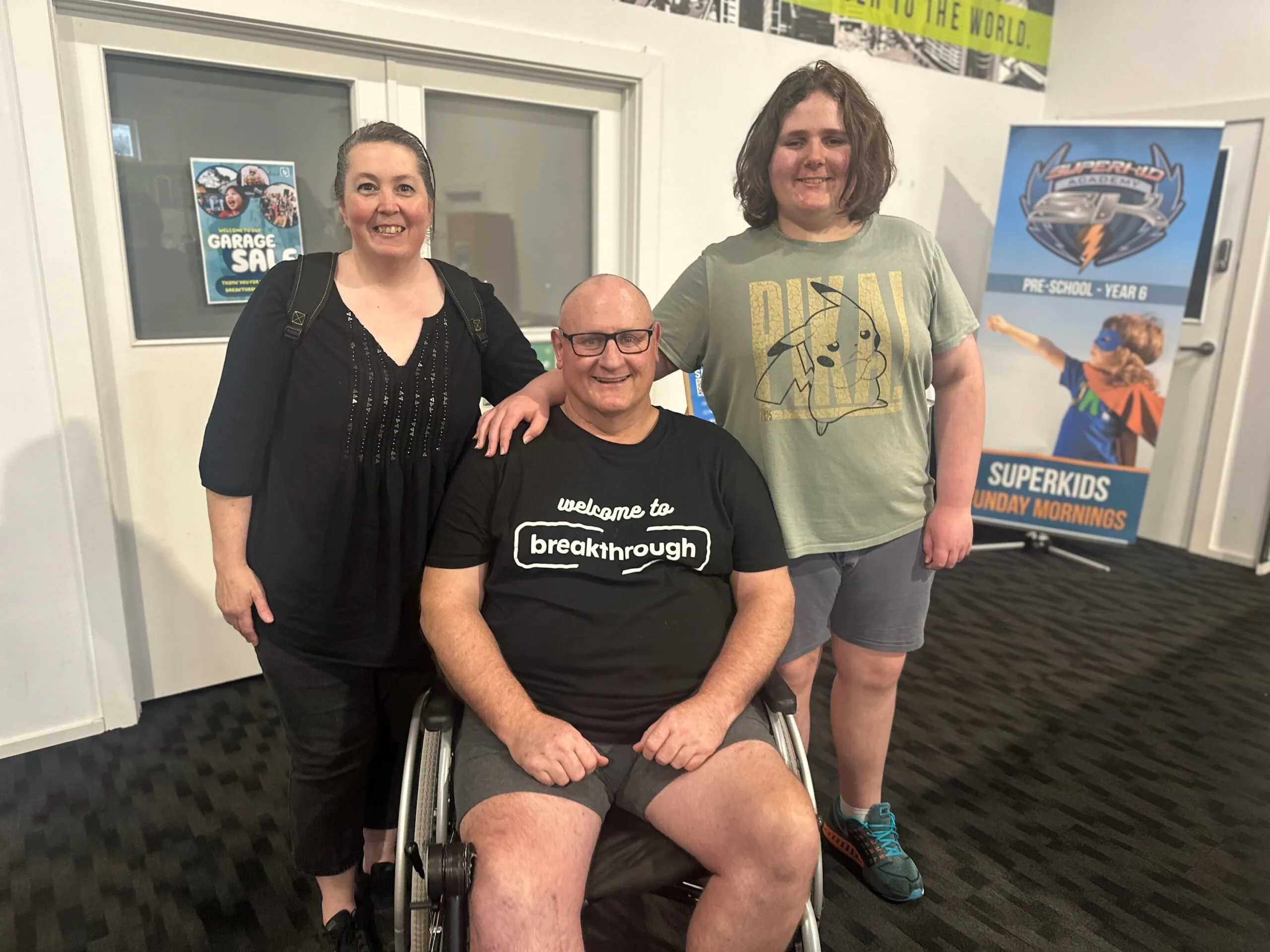 man in wheelchair with wife and son standing beside him