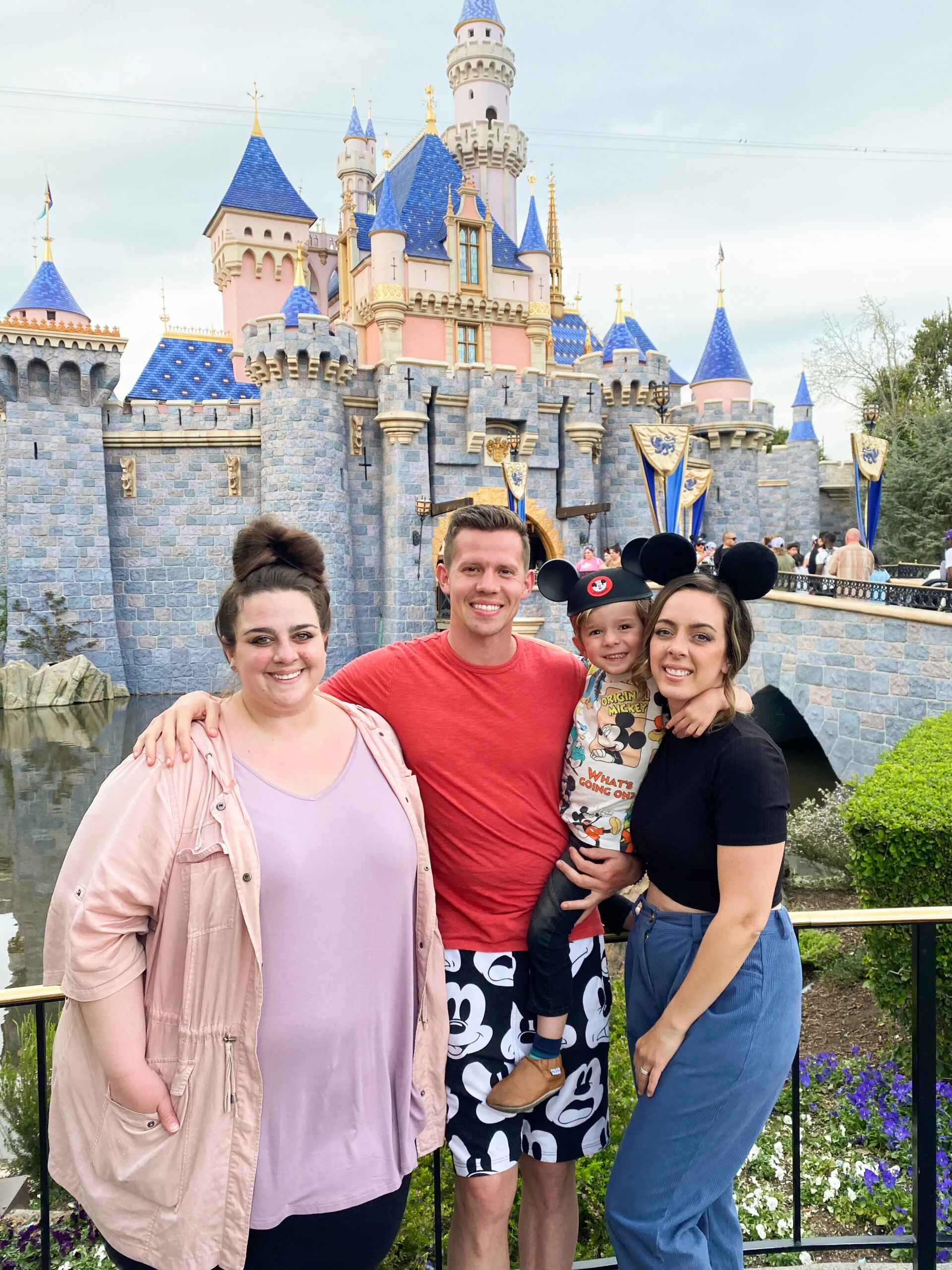 three adults and child in front of disney castle