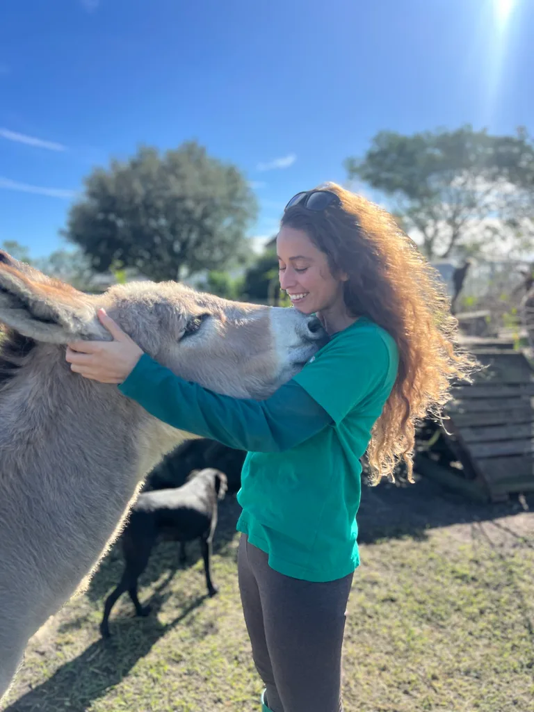 Image of woman wearing green top and hugging a donkey