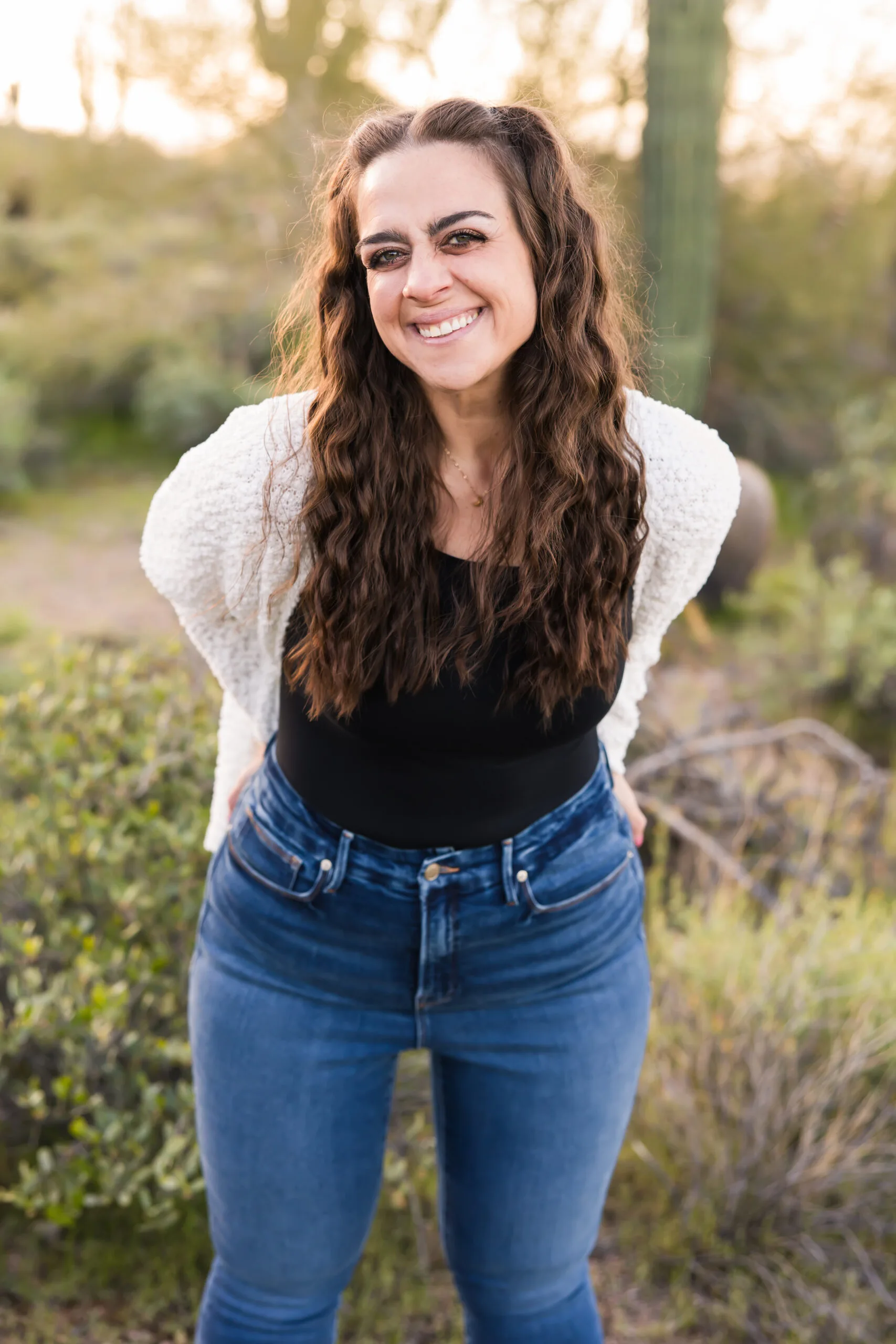 Woman in blue jeans and black top with white cardigan outside