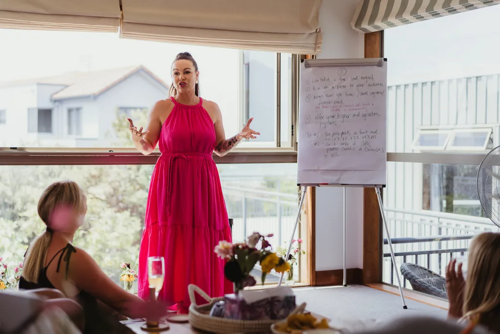 Libby speaking at her retreat. She is wearing a red dress and presenting to a group.
