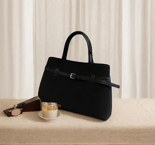 Black woman's bag on cream couch next to coffee and against a curtain background