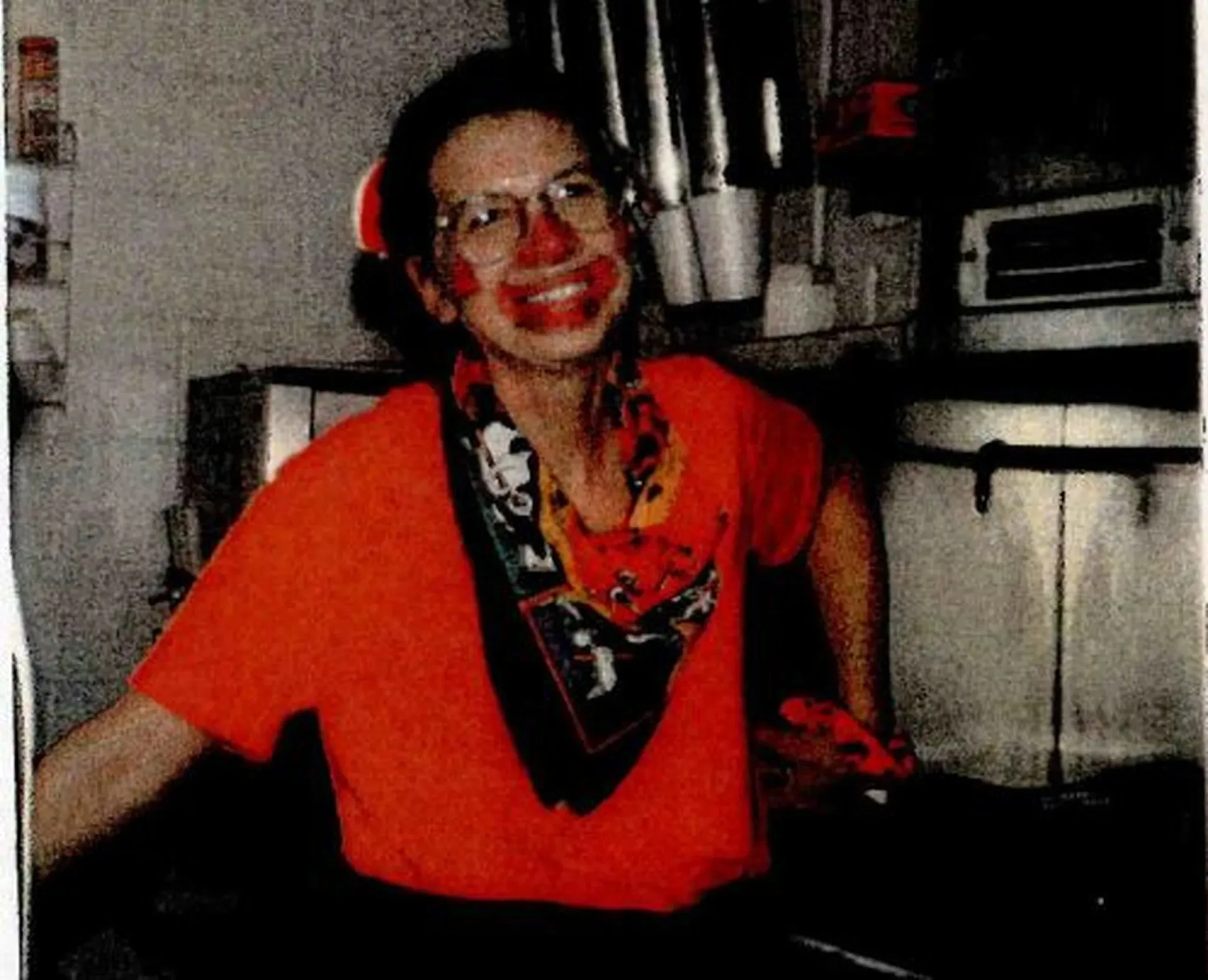 woman dressed in red with a scarf around her neck she has clown facepaint on and a red nose 