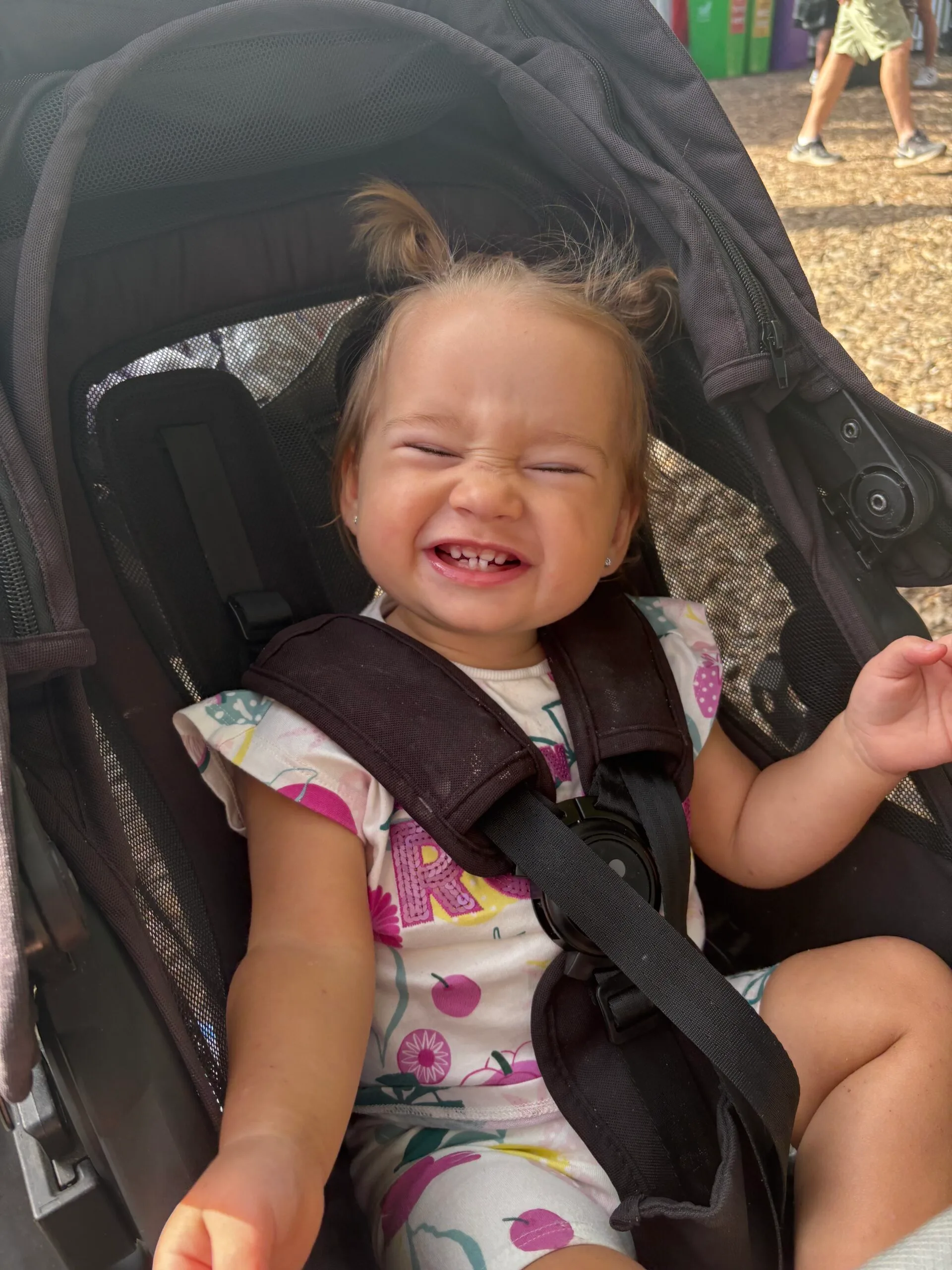Toddler in a pram, she is smiling widely and her hair is in pigtails