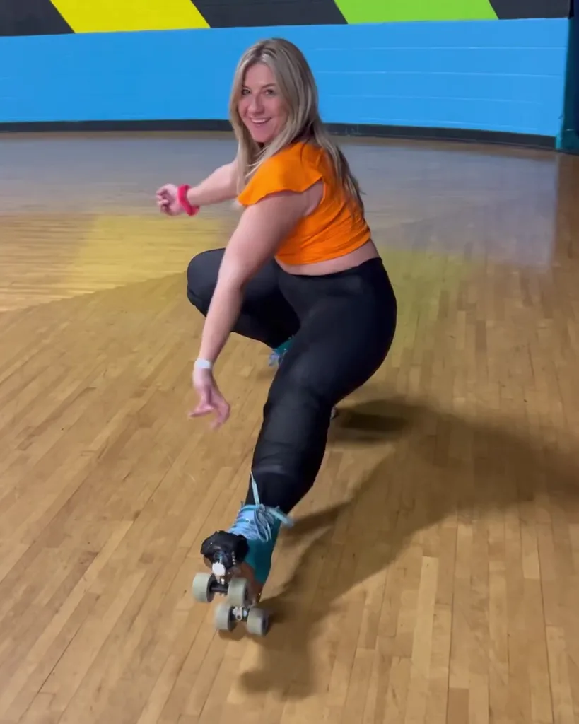 Connie after losing weight. She is rollerskating at the rink. She is wearing a cropped orange shirt, black tights and blue skates