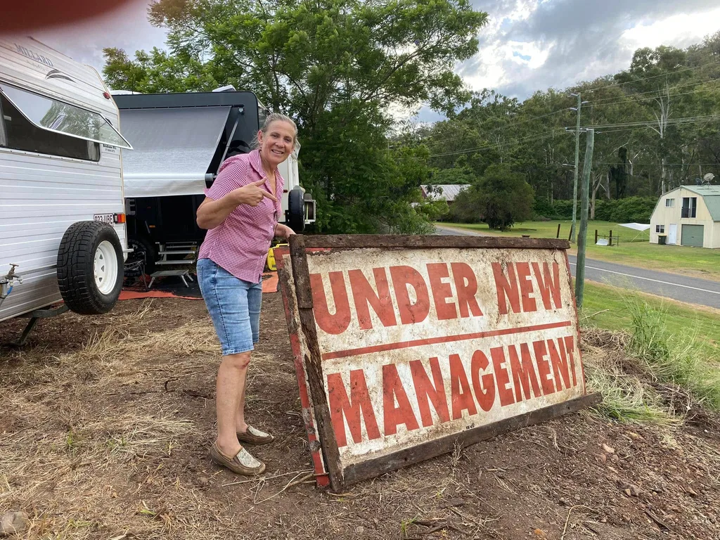 woman in front of a sign reading under new management in black and red in front of Tree