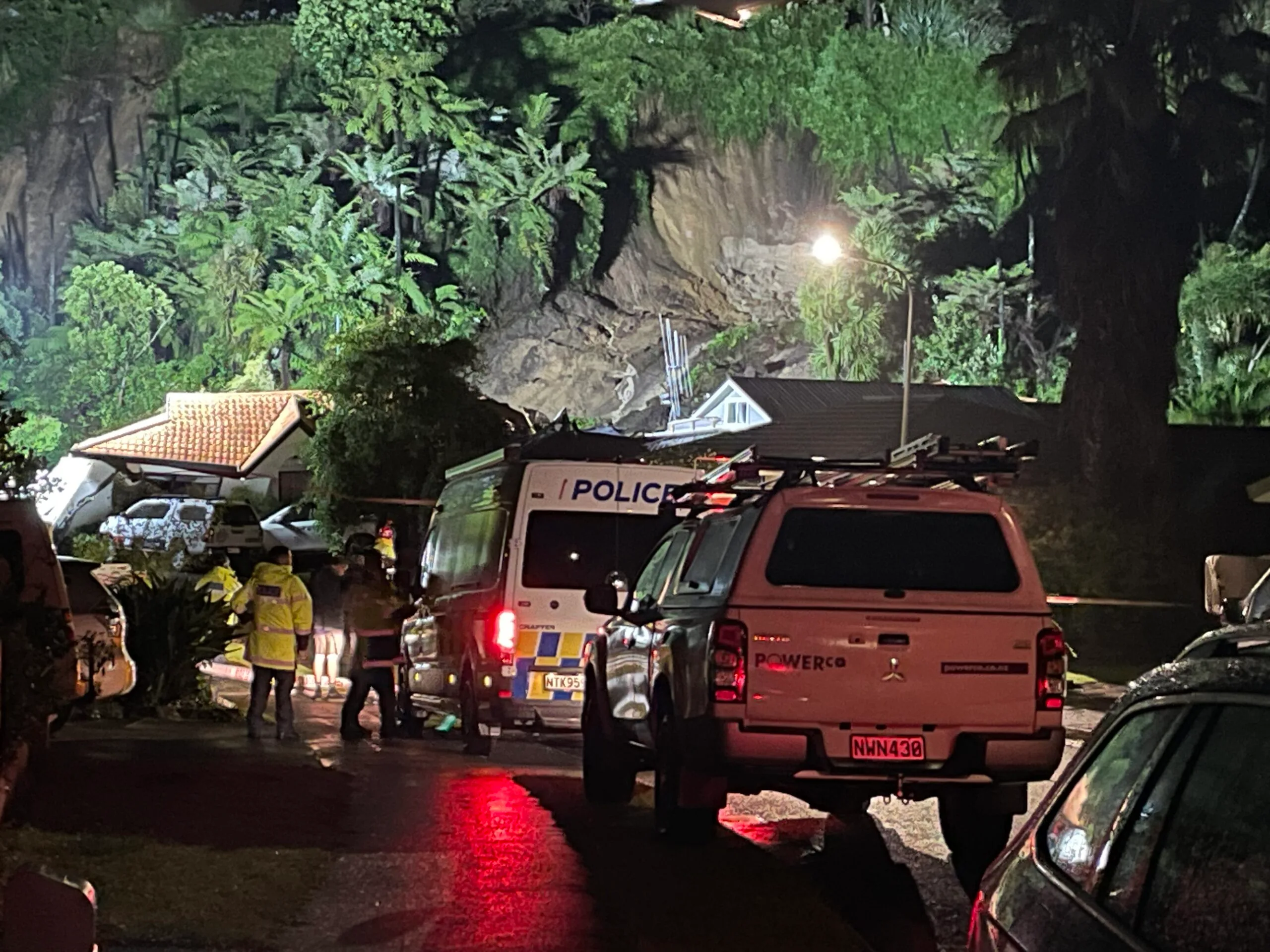 Landslide of mud and trees onto a huose with two utes and person standing in bright yellow top 