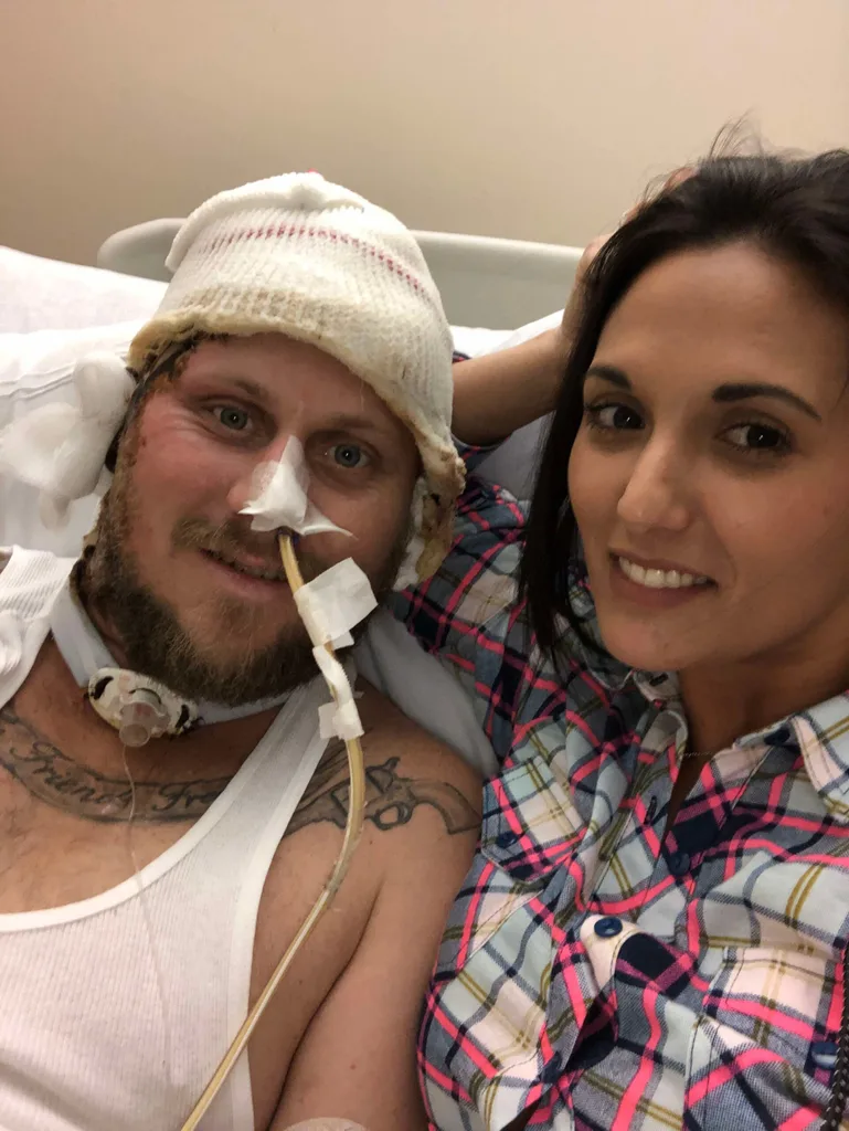 John awake in hospital. His head is covered in a bandage and he had a tube in his nose and throat. Tiffany is at his bedside.