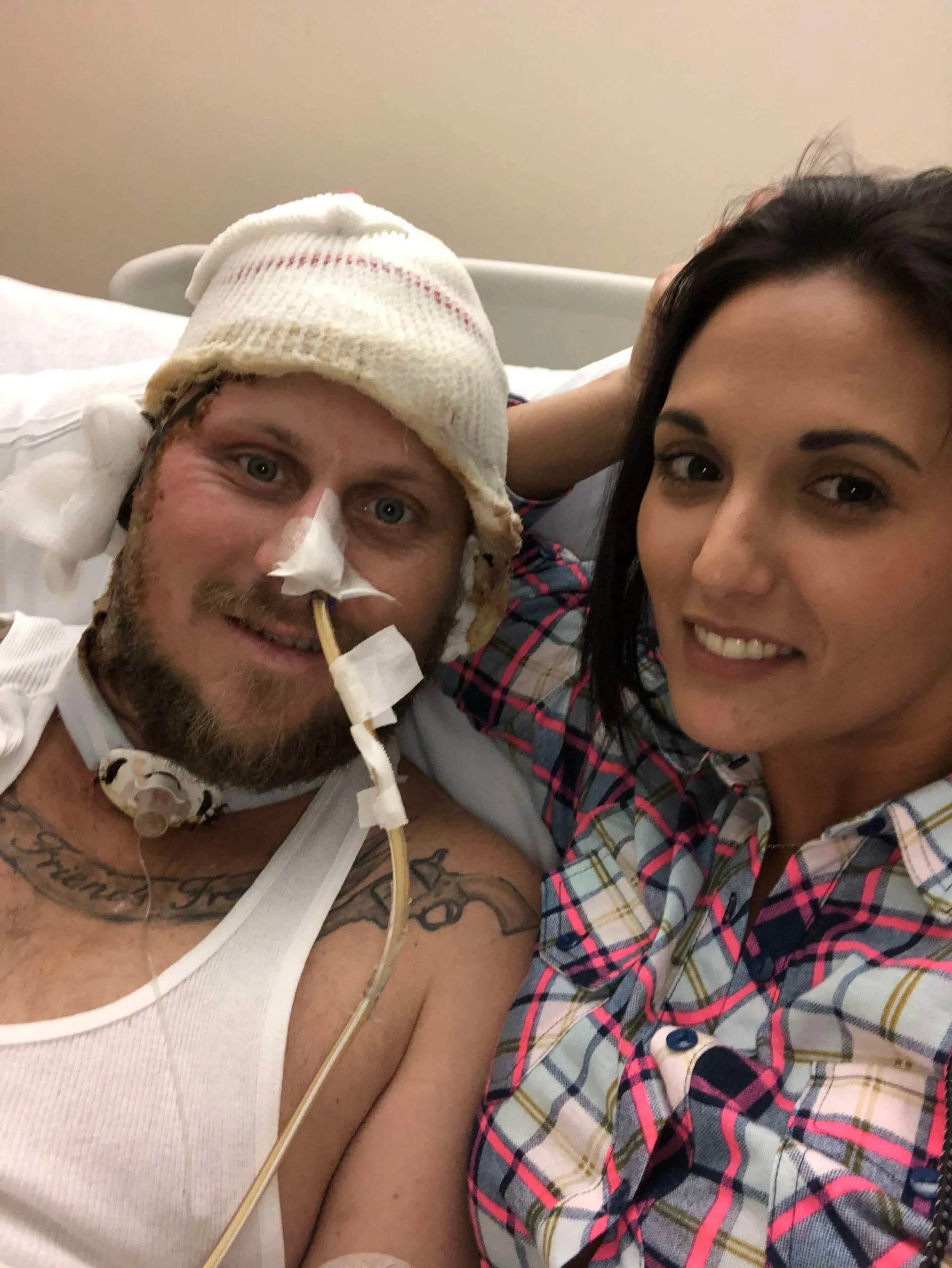 John awake in hospital. His head is covered in a bandage and he had a tube in his nose and throat. Tiffany is at his bedside.