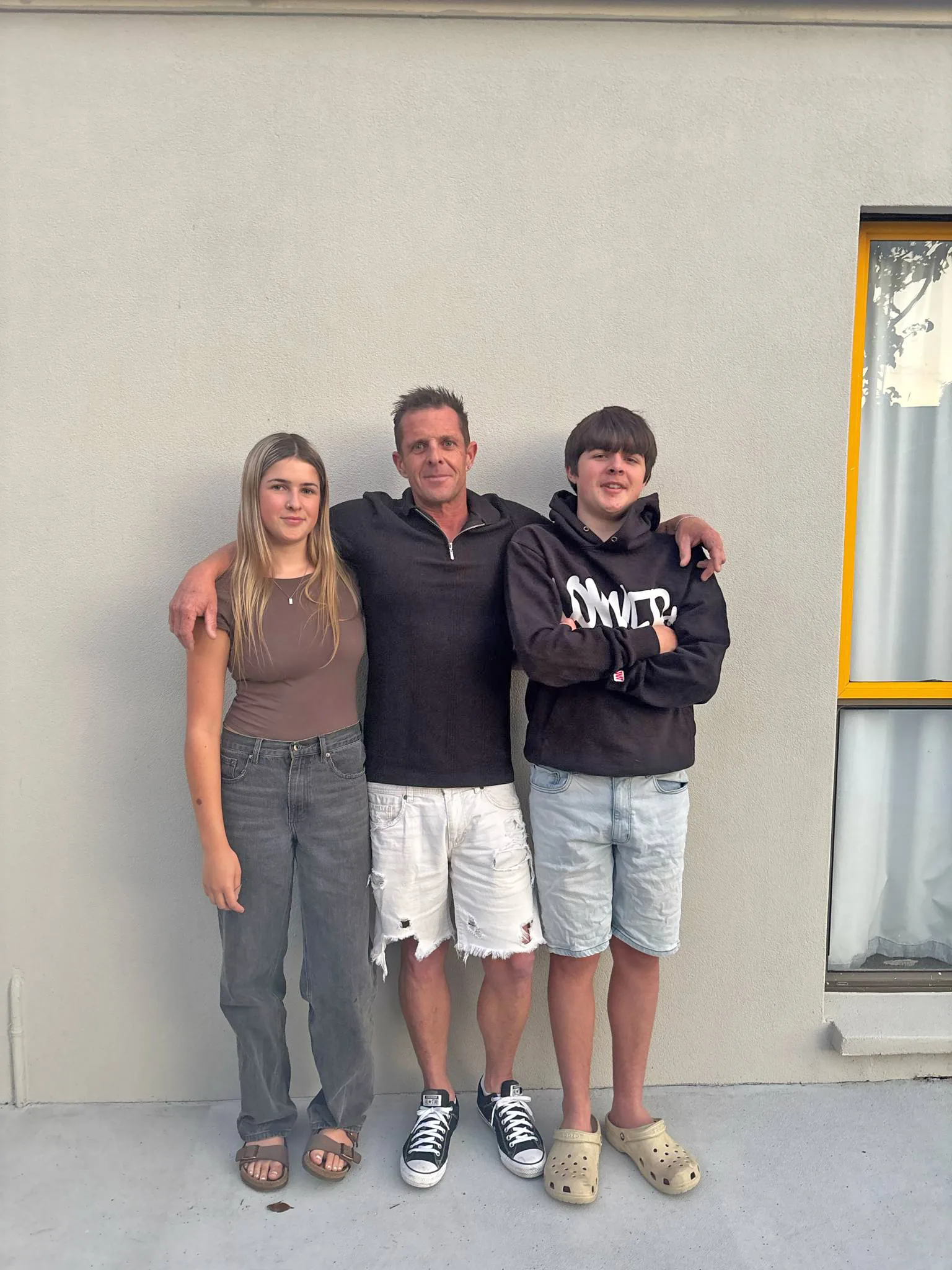 Man in black top white shorts, girl in grey trousres and brown top and boy in black tshirt and jean shirts