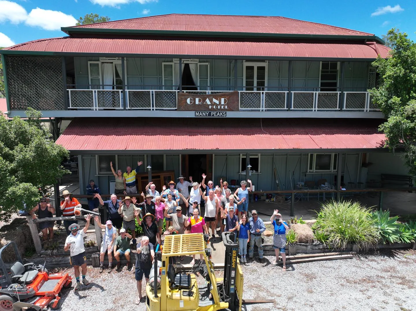 people in front of a pub with red roof amd yellow digger