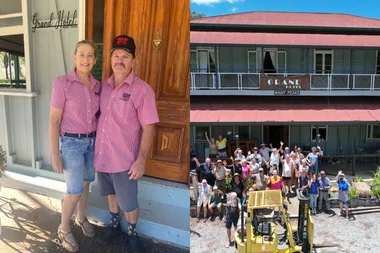 man and woman in paink tops in front of door and sign Grand hotel Photo of people outside hotel with a yellow digger.