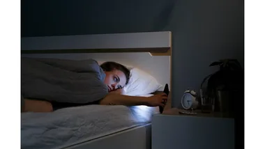 A wide awake woman checks her phone while in bed in the middle of the night.