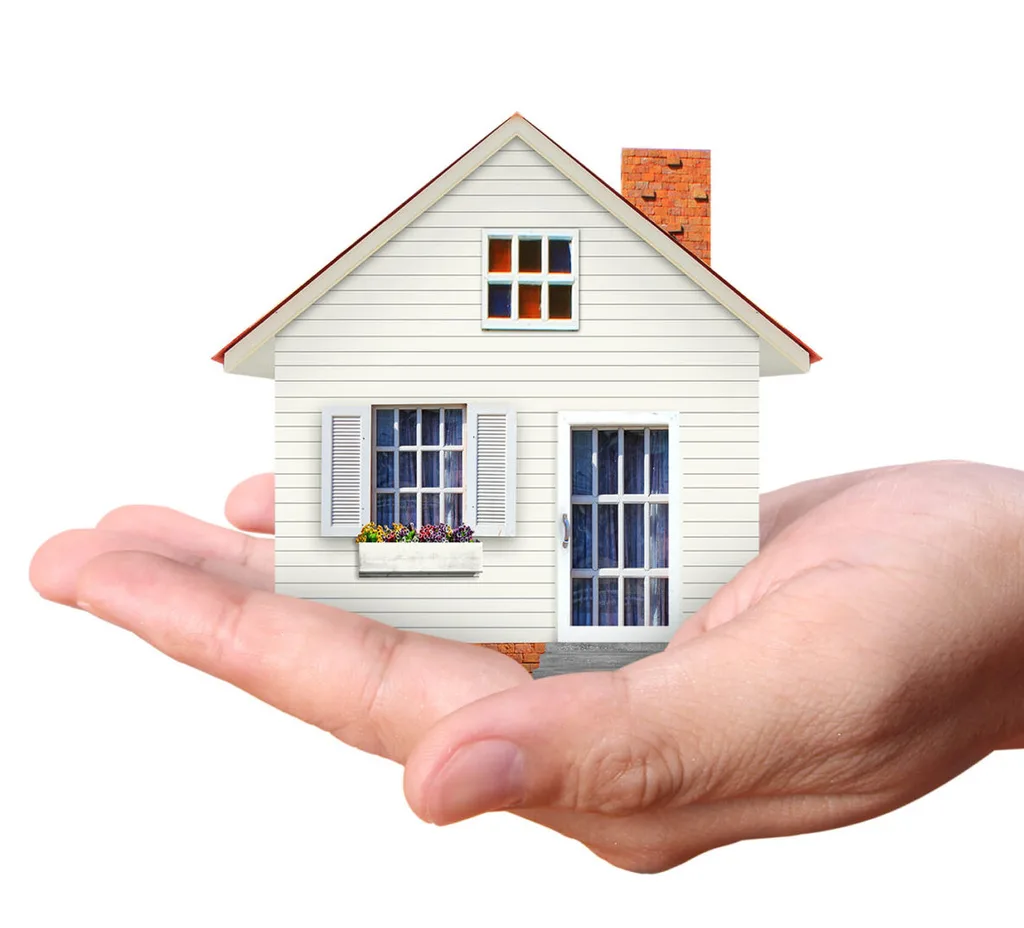 A hand holds a tiny white weatherboard house. It has two rustic windows and a brick chimney
