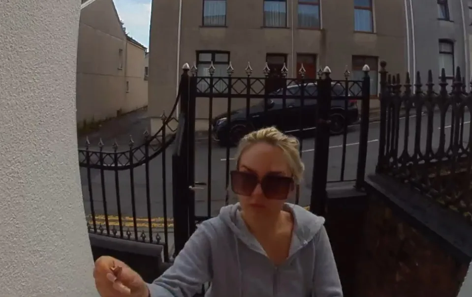 Woman in grey jumper and large sunglasses outside her home