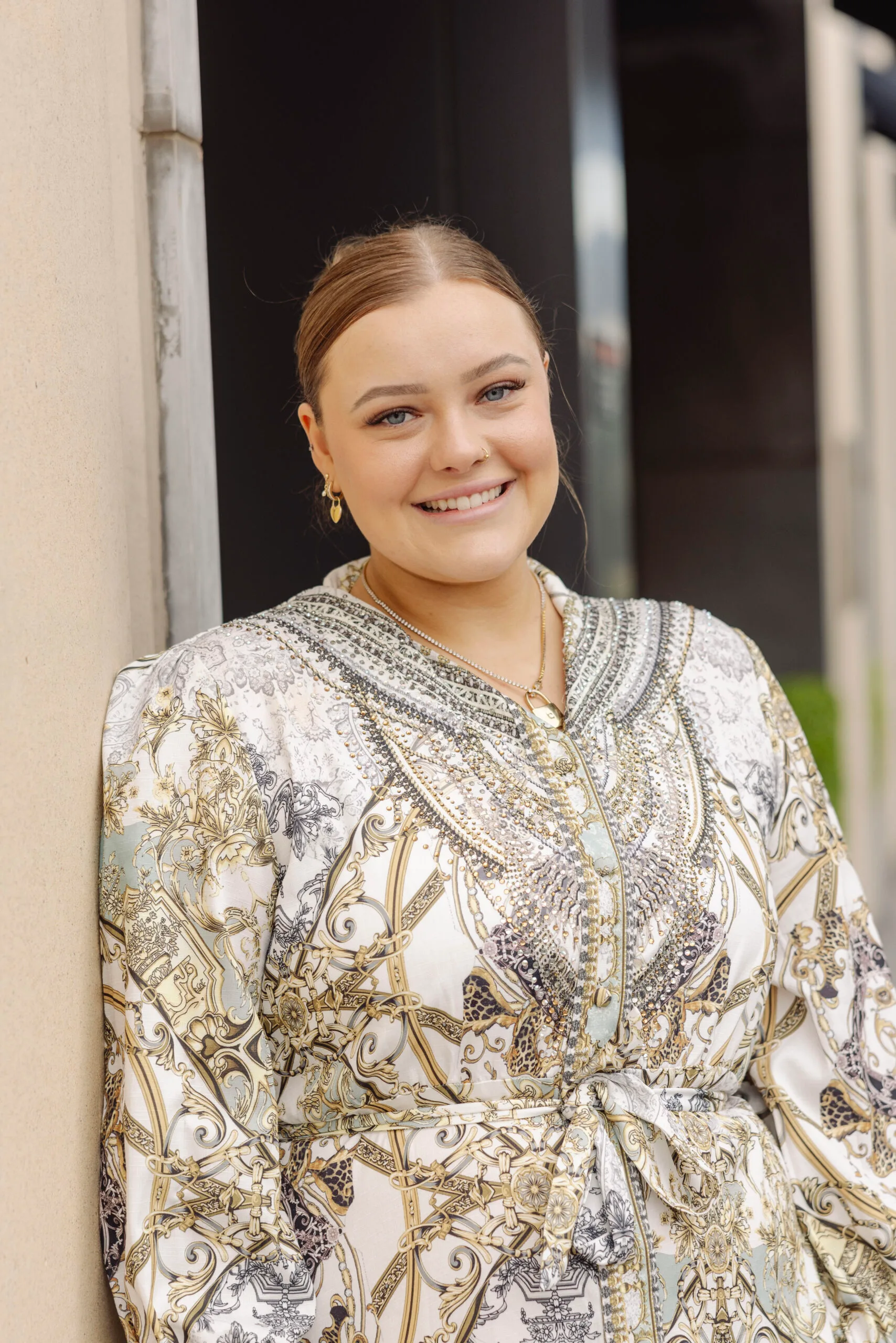 woman with hair pulled back smiling for the camera, she is wearing a gold and white paisley dress.