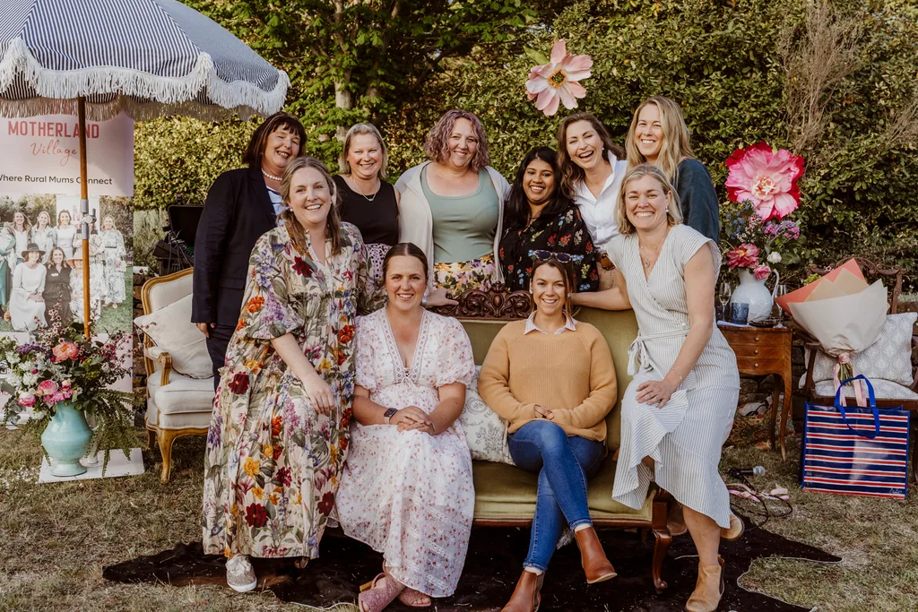 A group of women smiling at the camera. They are wearing smart casual attire and sitting or standing outside.