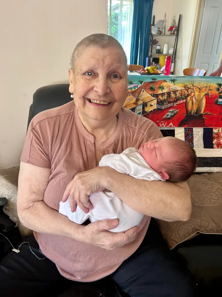 Image of woman wearing pink shirt and holding newborn baby in a white swaddle
