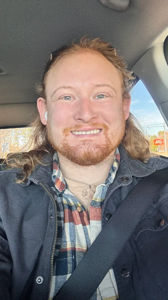 man sitting in car in black jacket and check shirt.