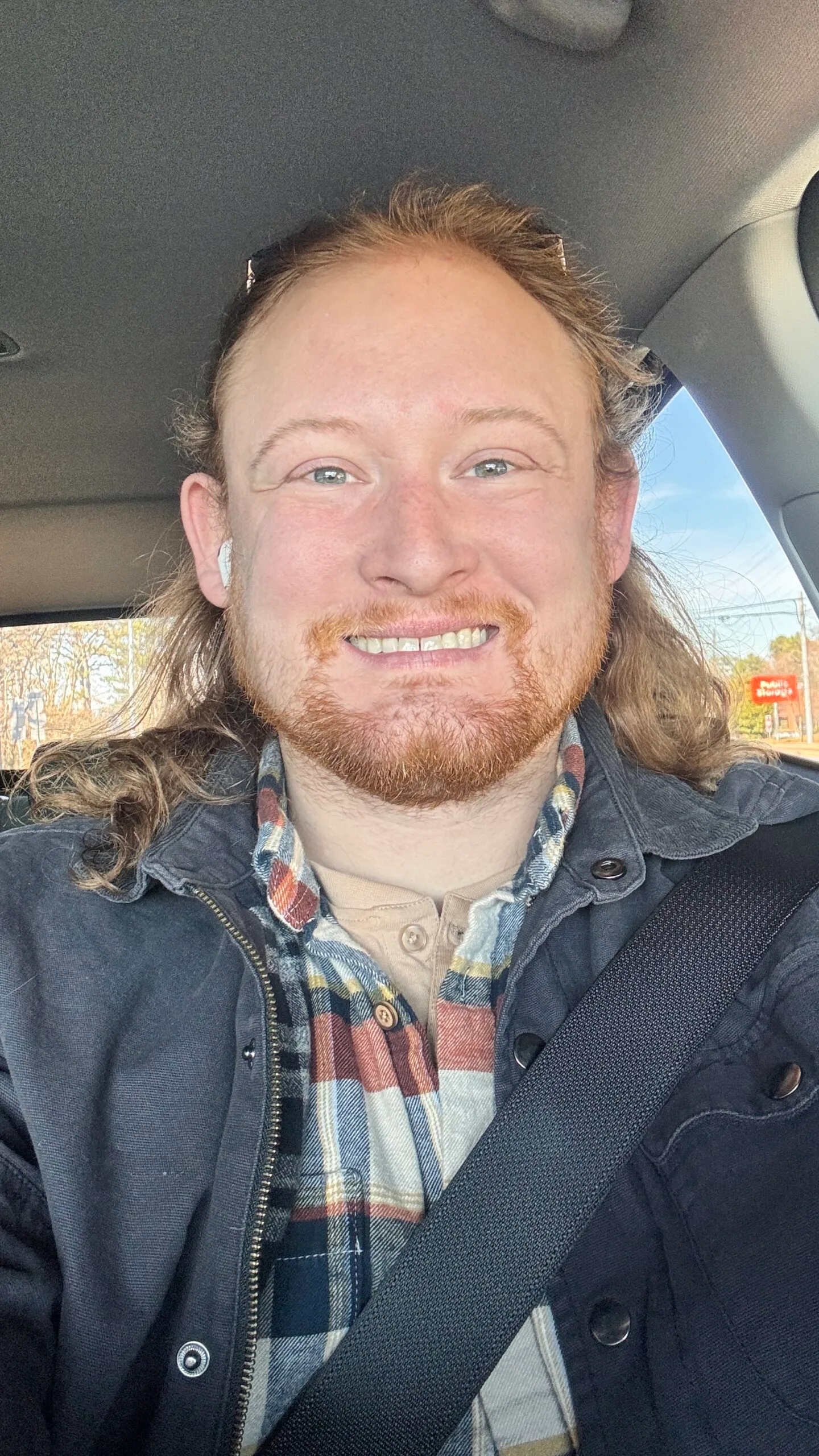 man sitting in car in black jacket and check shirt.
