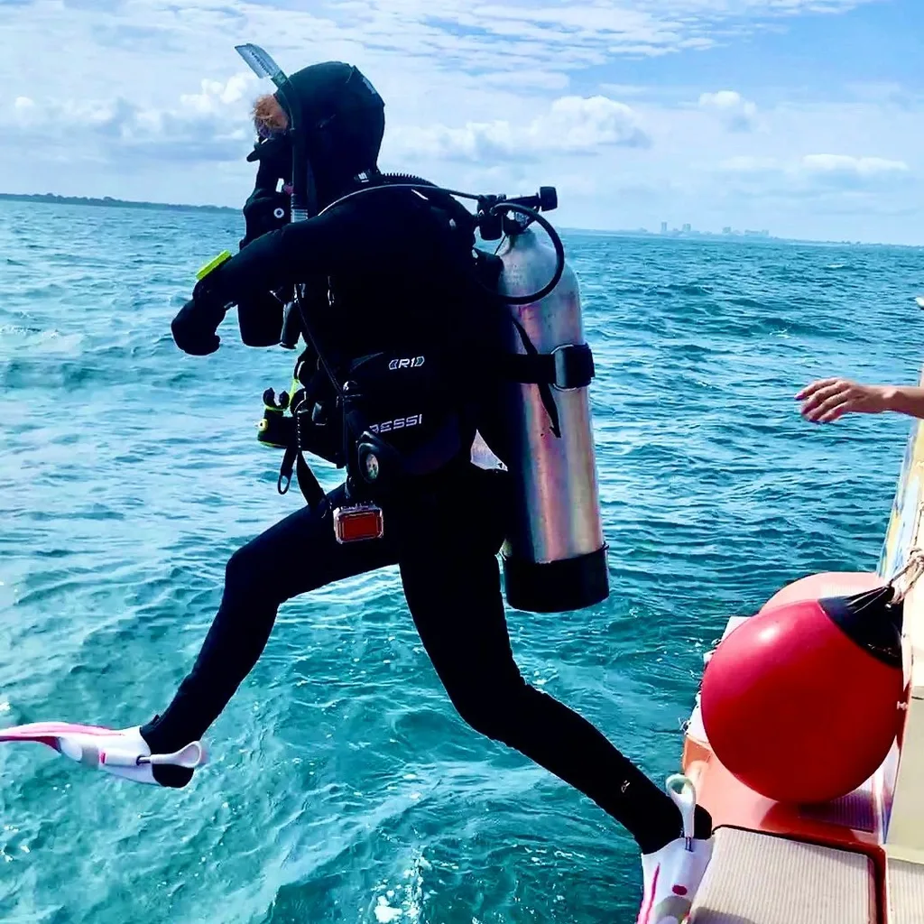 Image of woman jumping off edge of boat wearing scuba diving suit