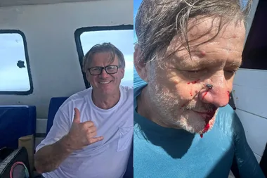 man in white tshirt on boat with thumbs up . man in blue top with white hair with blood n nose and chin