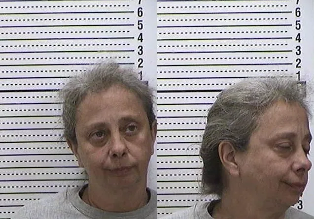 woman in front of police line-up wall, she is wearing a grey sweater.
