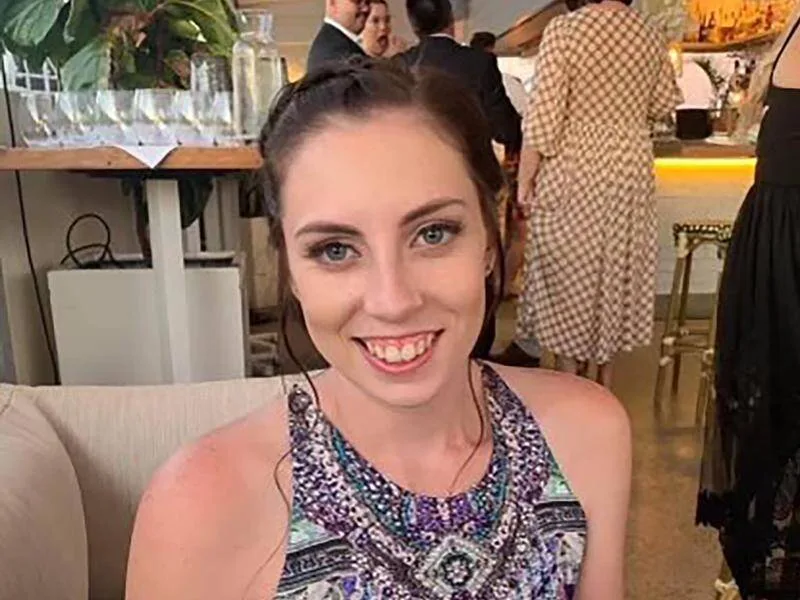 A woman smiles at the camera. She has brown hair and is wearing a colourful top