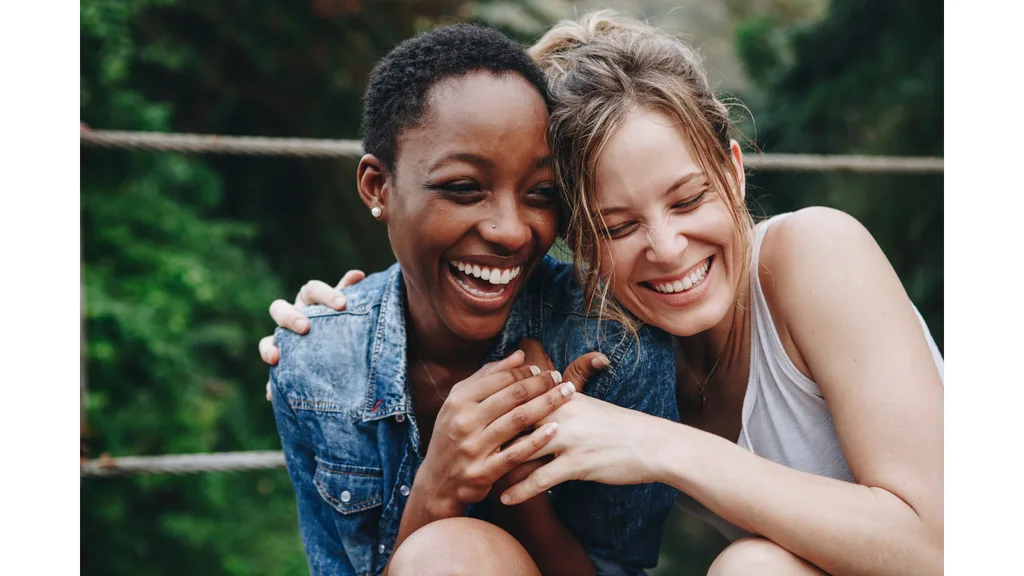 Two young female friends share a laugh and a hug.