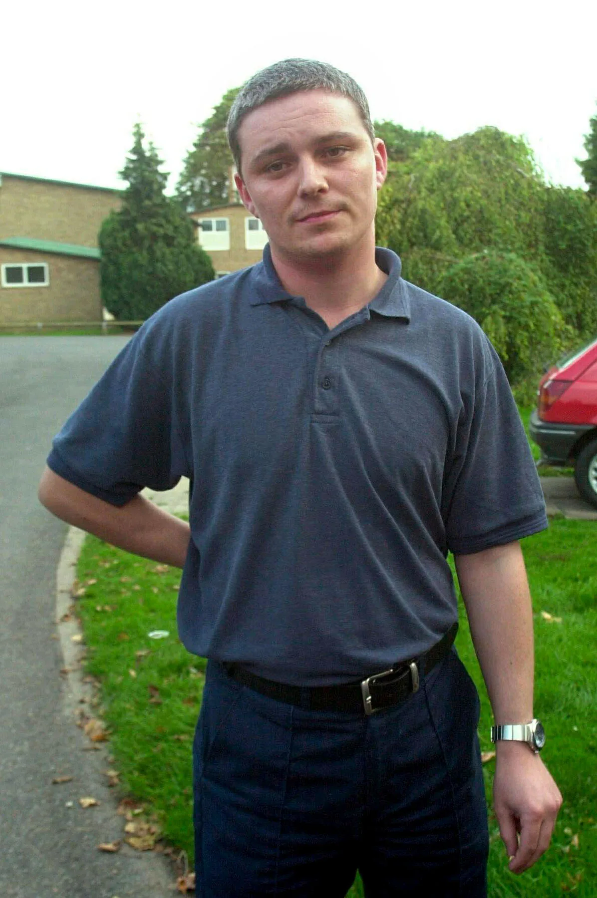 Ian Huntley in dark polo shirt and black trousers stands outside