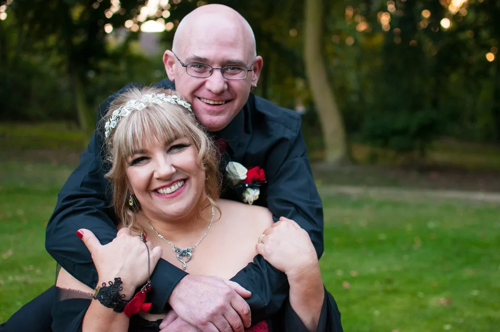 woman in suit holding woman with blonde hair standing outside in front of tree on grass