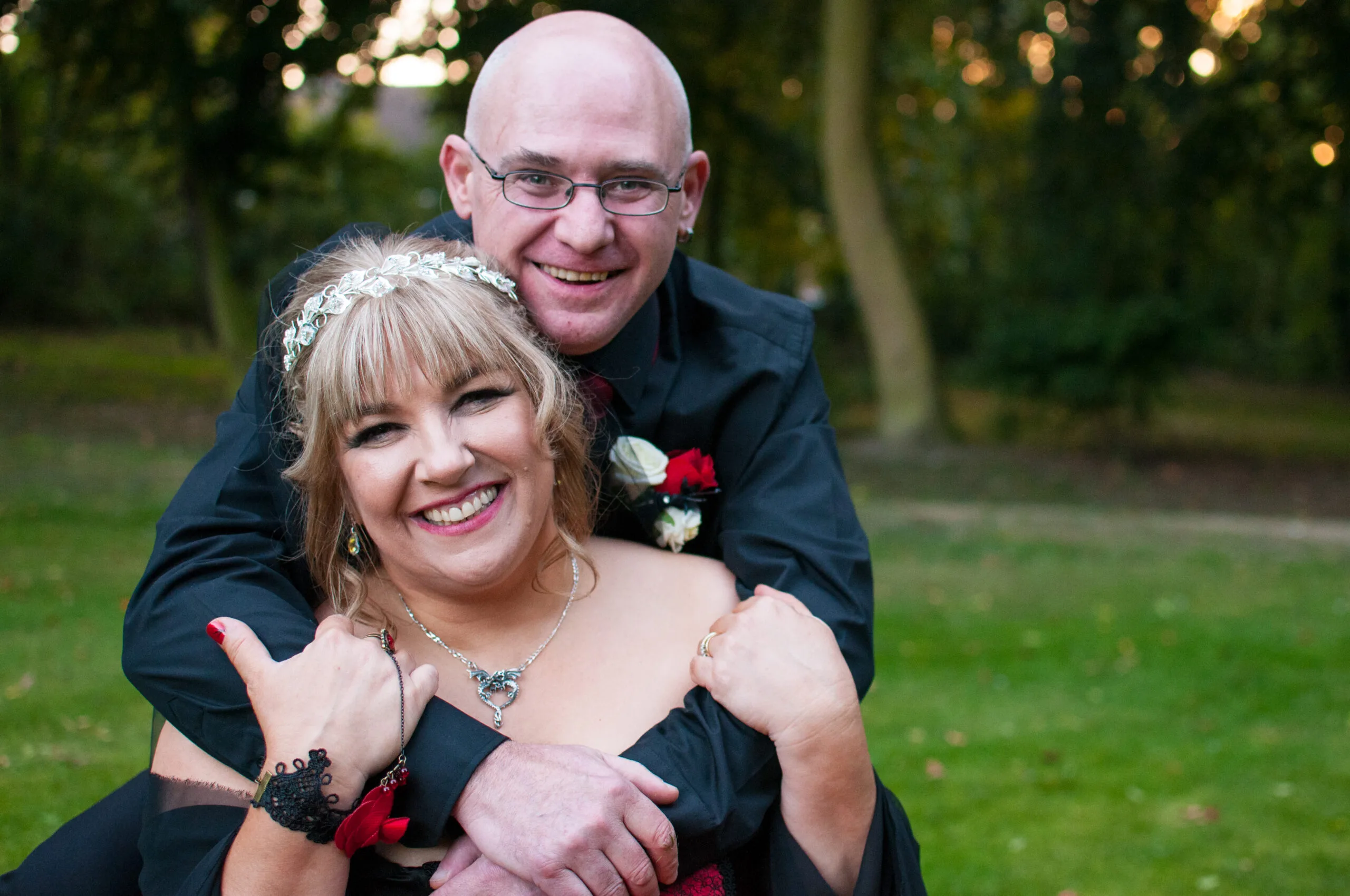 woman in suit holding woman with blonde hair standing outside in front of tree on grass
