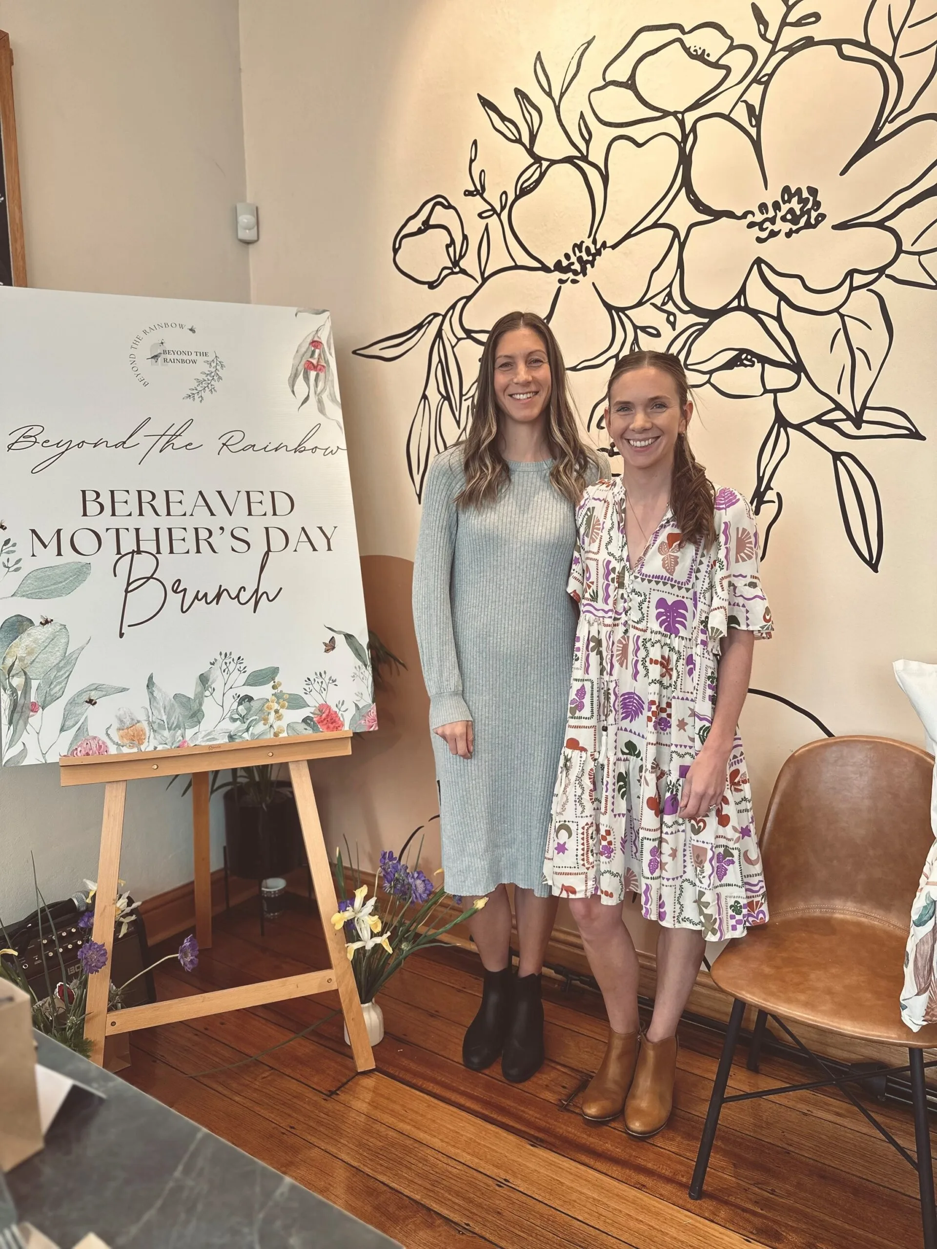 two women standing beside a board reading bereaved mothers day brunch