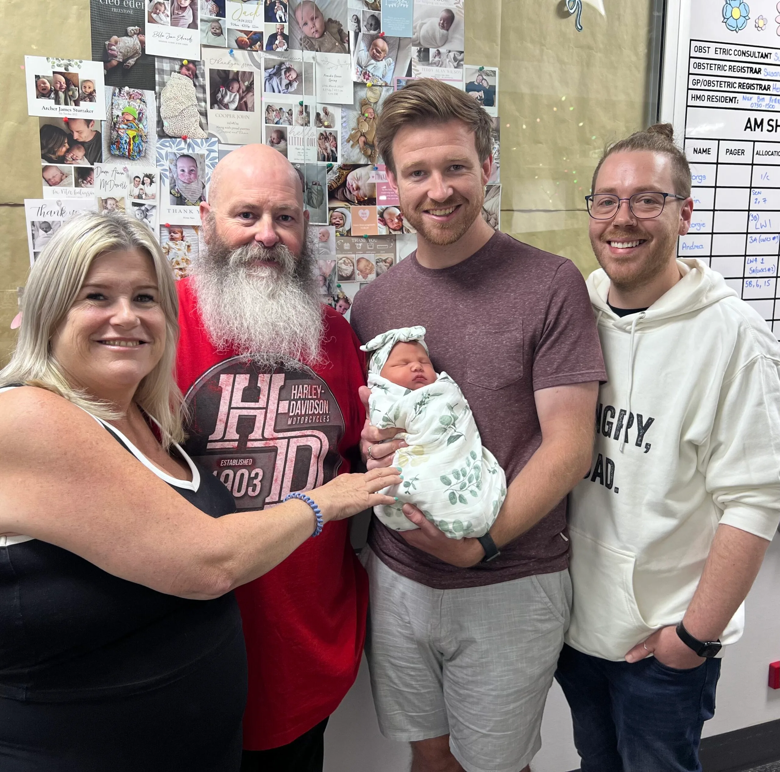 Four people smile for the camera while holding a baby