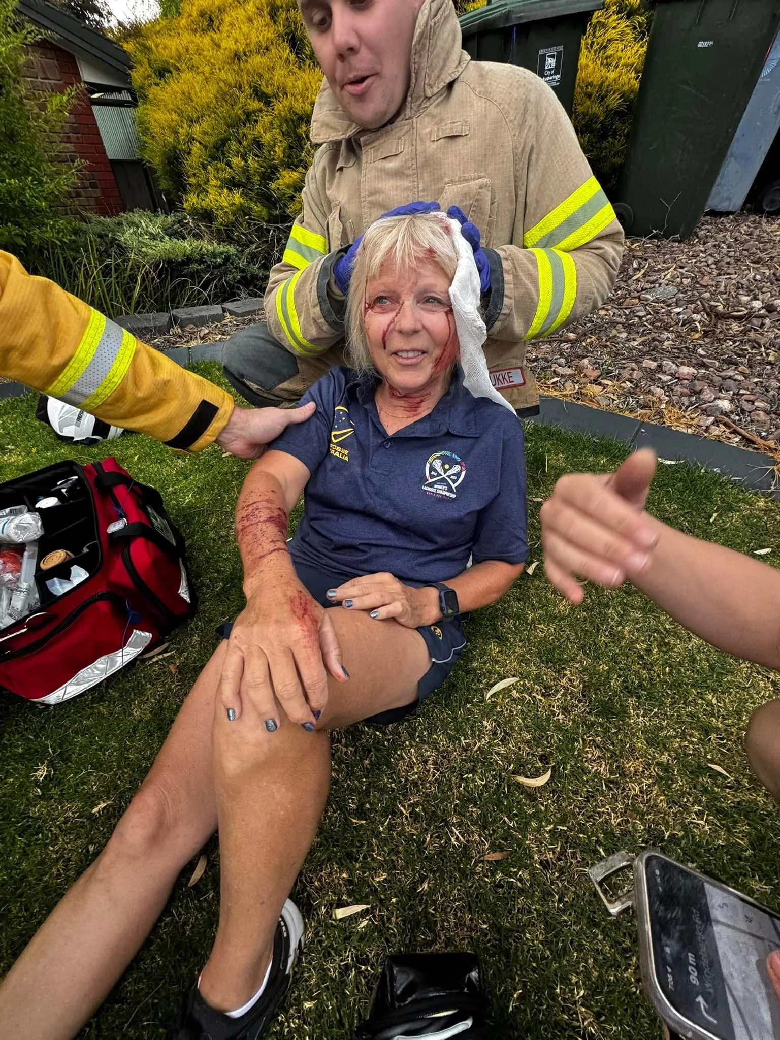 Marilyn suffering from her injuries post accident. She is sitting on the grass and being attended to by emergency service crew.